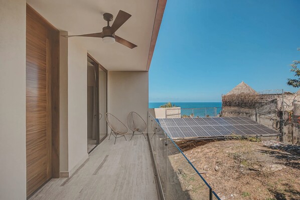 Un balcon doté d’un ventilateur de plafond, de deux chaises en fil de fer et de panneaux solaires.