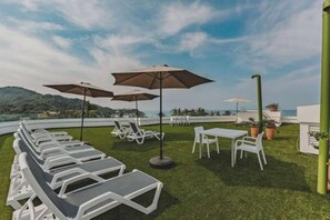 A rooftop terrace with lounge chairs and umbrellas, offering a view of the sea and hills. - Vista Verde at La Esquina: San Pancho 2BR, Rooftop Views, 1 Block to Beach (San Pancho)