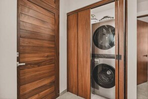 Ein Holzschrank mit Spiegel und Glastür, der eine Waschmaschine und ein Regal mit darin befindlichen Gegenständen zeigt.
