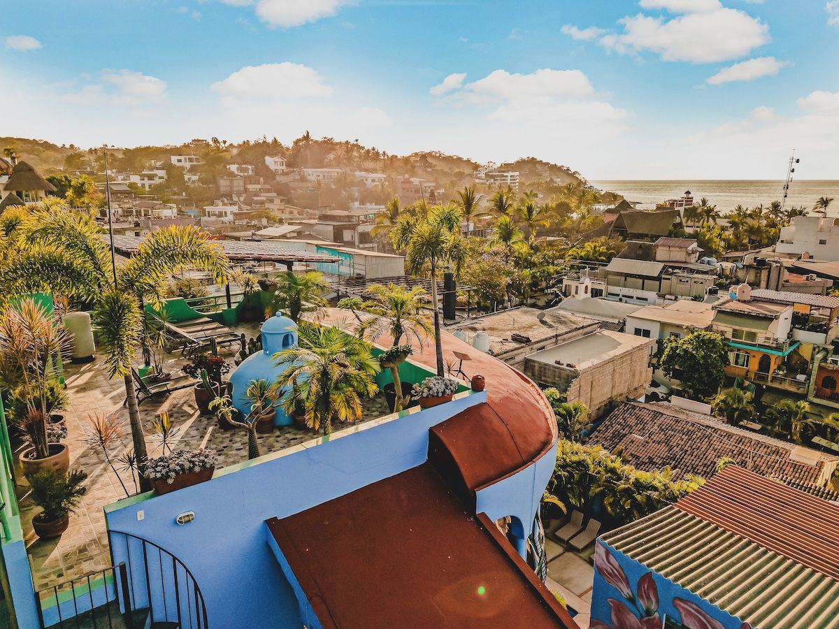 A residential area with a blue building, palm trees, and a view of the sea.
