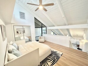 Ein Schlafzimmer mit Bett, Deckenventilator, Fenster und Blick ins Freie.