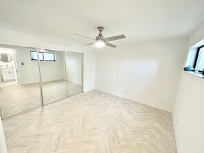 Ein Zimmer mit einem Fischgrätparkett, einem Deckenventilator und einer Schiebetür zu einem Badezimmer.