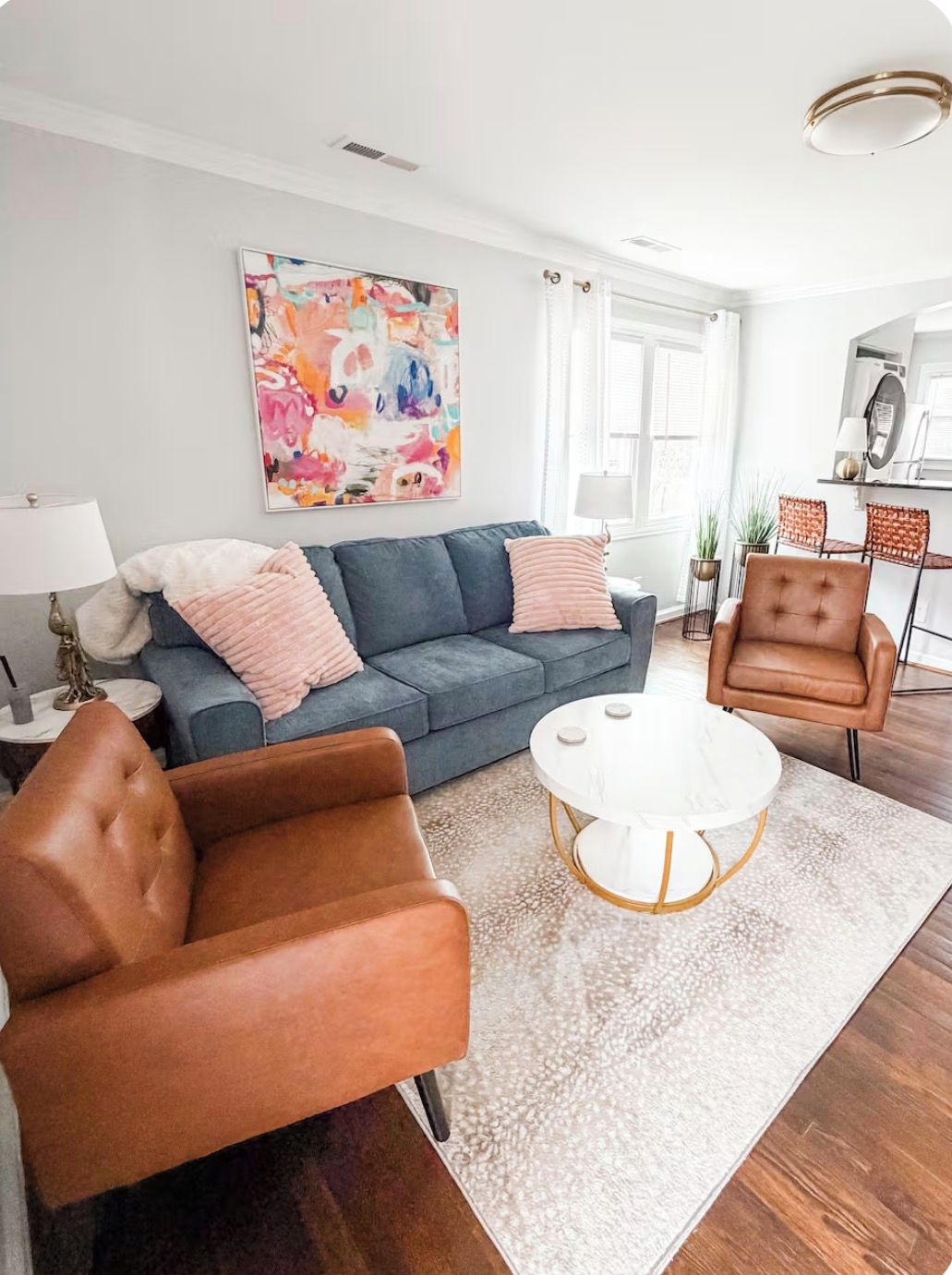 Un salon avec un canapé gris, un fauteuil en cuir marron, une table basse blanche et un tableau abstrait aux couleurs vives accroché au mur.