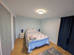 Een slaapkamer met een bed, nachtkastjes, een hanglamp en een raam met gordijnen.