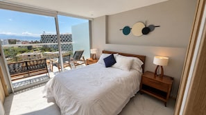 A bedroom with a large bed, two bedside tables with lamps, a view of the city through a balcony, and a wall art piece. - New Listing (Bucerías)
