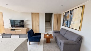 A modern living room with a flat-screen TV, a blue chair, a grey sofa, and a coffee table. - New Listing (Bucerías)