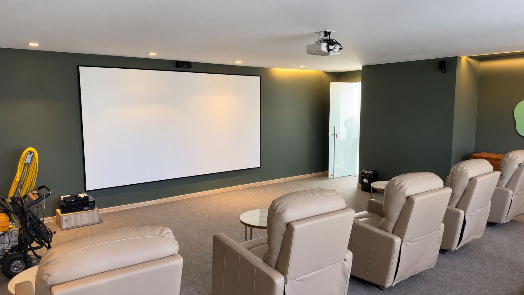Sala de cine en casa con televisor de pantalla grande, butacas reclinables, un proyector y piso alfombrado.