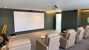 Une salle de cinéma privée équipée d’un grand téléviseur à écran plat, de fauteuils inclinables, d’un projecteur et d’un sol recouvert de moquette.