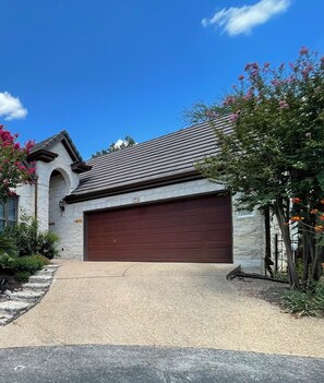 A residential house with a garage, stone facade, and a clear sky. - 3-2.5 house in gated Westlake Hills w/pool, heated spa, fenced yard & EV charger (Austin)