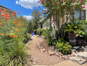 A garden pathway leading to a building with a pergola, surrounded by various plants and trees. - 3-2.5 house in gated Westlake Hills w/pool, heated spa, fenced yard & EV charger (Austin)