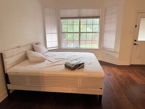 Un dormitorio con una cama grande, una ventana con persianas, una puerta y suelo de madera.