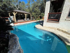 Una piscina con solárium de piedra, un porche cubierto y un edificio de piedra con balcón.