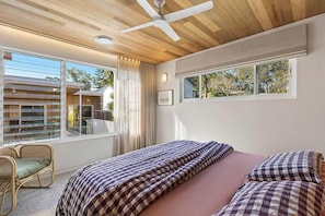 A bedroom with a bed, a ceiling fan, a window with curtains, and a view of the outside. - Paradise Club by Coast Hosting (Wamberal)