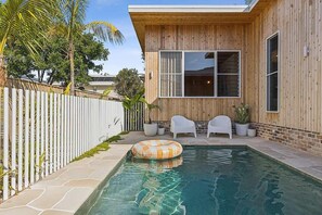 A swimming pool with a wooden deck, white chairs, and a white fence. - Paradise Club by Coast Hosting (Wamberal)