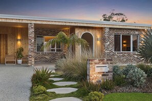 A modern house with a brick exterior, a wooden porch, and a well-maintained garden with stepping stones. - Paradise Club by Coast Hosting (Wamberal)
