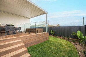 Eine moderne Außenpatio mit Holzterrasse, Glasveranda und einem Rasenstück.