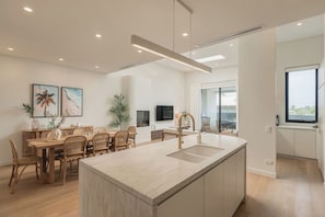 Une cuisine moderne dotée d’un îlot central, d’un coin repas avec des chaises en osier et d’une grande fenêtre offrant une vue dégagée.