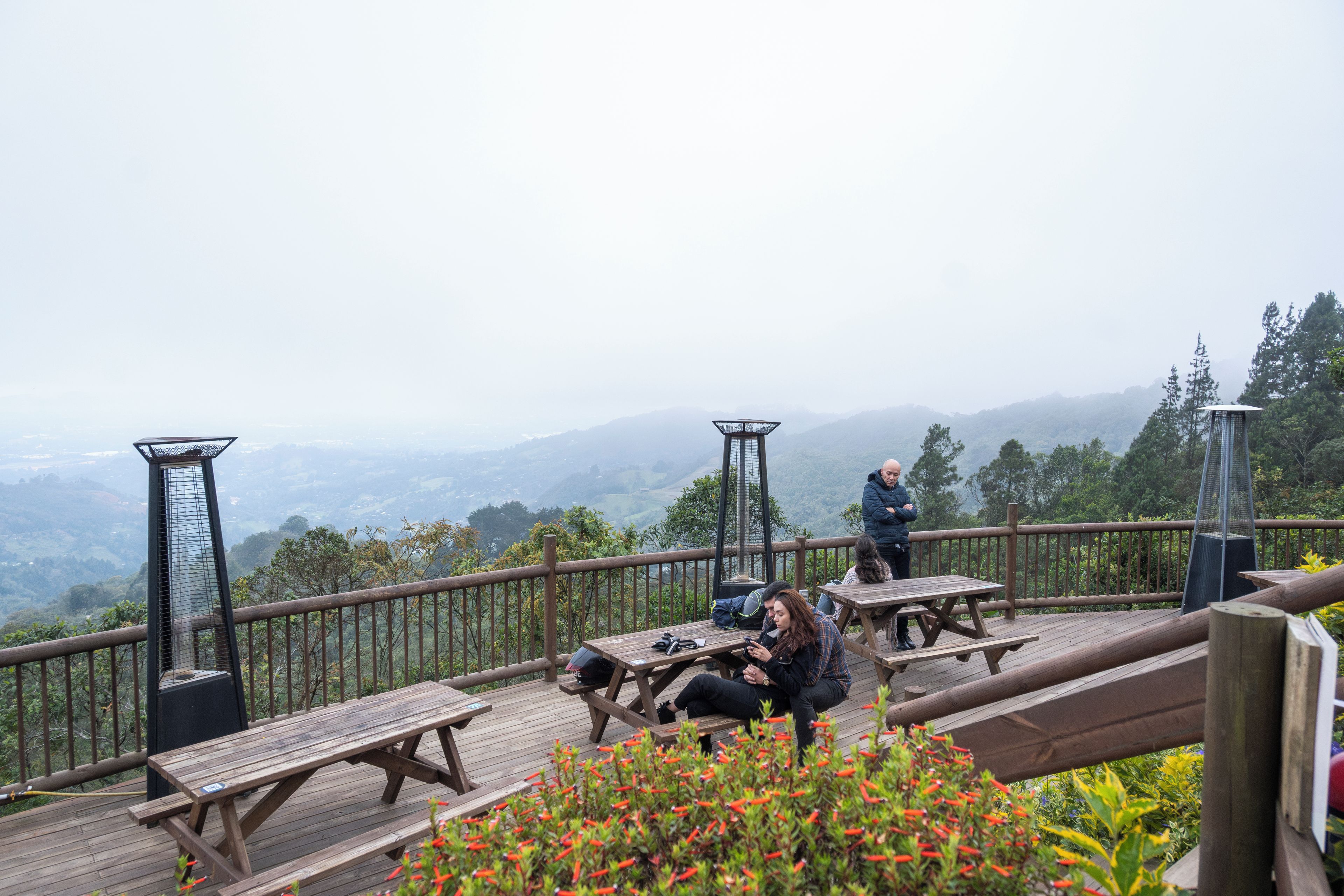 Una terraza de madera con mesas de picnic con vistas a un paisaje montañoso.