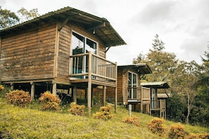 A wooden cabin with a balcony, surrounded by natural vegetation.