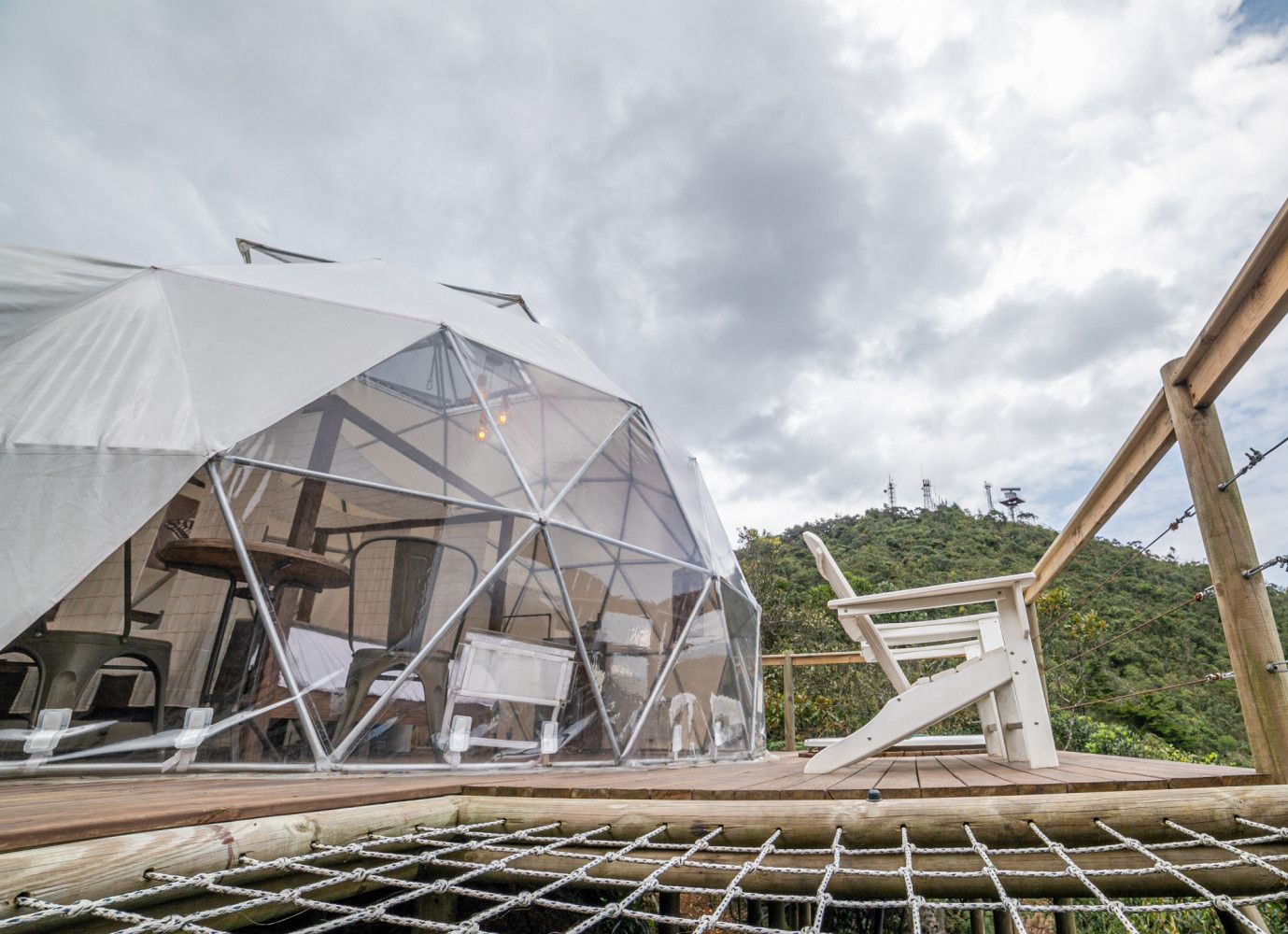 Estructura de cúpula geométrica con techo transparente, plataforma de madera y una silla.