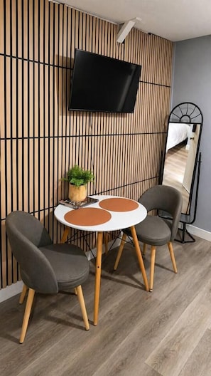 A modern room with a flat-screen TV mounted on a wooden slat wall, a round table with two chairs, and a large mirror on the wall. - 2 Studios + 2BR Home Near Whiskey Row (Prescott)