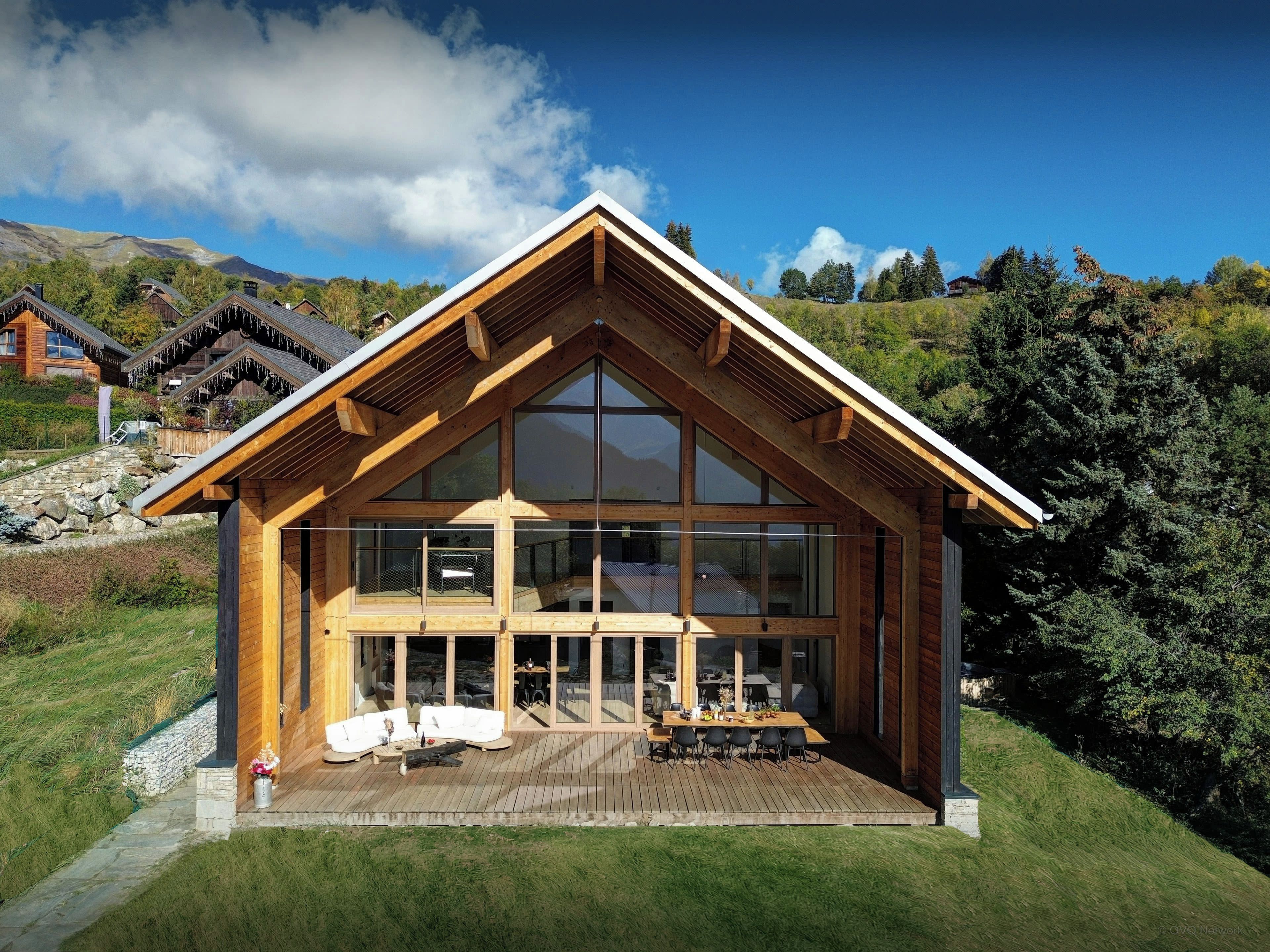Una baita di legno con ampie finestre, una terrazza e uno scenario montuoso.