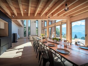 Un comedor amplio con una larga mesa de madera, varias sillas y ventanas grandes con vistas a la montaña.