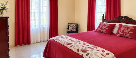 Een slaapkamer met een bed, gordijnen, een stoel en een houten dressoir.