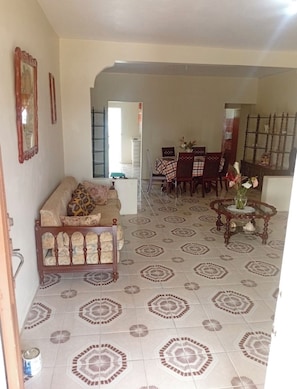 A living room with a sofa, dining table, chairs, and patterned floor tiles. - Private 4BD/3BAHome Near Black River Safari, YS Falls & Hospital (St. Elizabeth Parish)