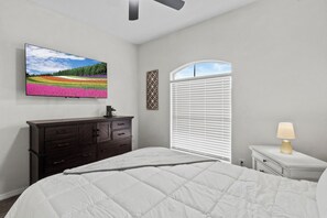 A bedroom with a bed, a dresser, a TV on the wall, a window with blinds, and a nightstand with a lamp. - Spacious 4BR 3BA 2 masters bedroom  TVs in every room (El Paso)
