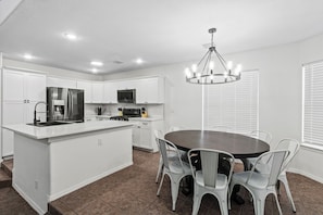 A modern kitchen with white cabinetry, a central island, and a dining area with a round table and chairs. - Spacious 4BR 3BA 2 masters bedroom  TVs in every room (El Paso)