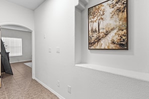 A hallway with white walls, a framed painting, and a door leading to another room. - Spacious 4BR 3BA 2 masters bedroom  TVs in every room (El Paso)