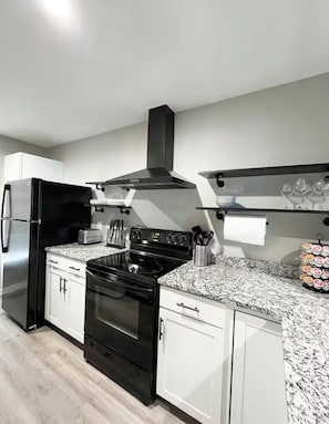 A modern kitchen with a black stove, white cabinets, and a granite countertop. - Cozy Townhome in the Perfect location! (Columbia)
