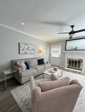 Una sala de estar con sofá, sillones, una mesita de centro, lámpara, ventilador de techo y chimenea.