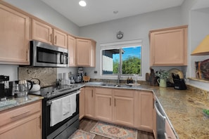 A modern kitchen with stainless steel appliances, wooden cabinets, and a window with a view of greenery. - Oro Valley 2BR Condo with Pool-View Balcony, Shared Pool & Hot Tub (Oro Valley)