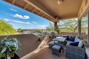 A covered outdoor seating area with a view of a swimming pool and buildings in the background. - Oro Valley 2BR Condo with Pool-View Balcony, Shared Pool & Hot Tub (Oro Valley)