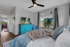 A bedroom with a bed, a ceiling fan, a window with curtains, a painting on the wall, and a view of the outdoors. - Oro Valley 2BR Condo with Pool-View Balcony, Shared Pool & Hot Tub (Oro Valley)