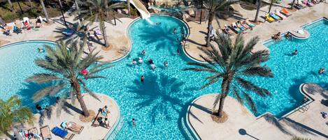 Una amplia piscina exterior con varias pistas de natación, rodeada de palmeras y tumbonas.