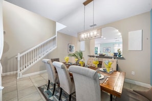 A dining area with a wooden table, grey upholstered chairs, and a chandelier. - BRAND NEW | Solterra Home, Pool + Spa & Game Room 5184 (Davenport)