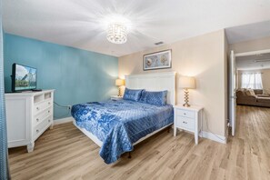 A bedroom with a bed, bedside tables, a television, and a door leading to another room. - BRAND NEW | Solterra Home, Pool + Spa & Game Room 5184 (Davenport)