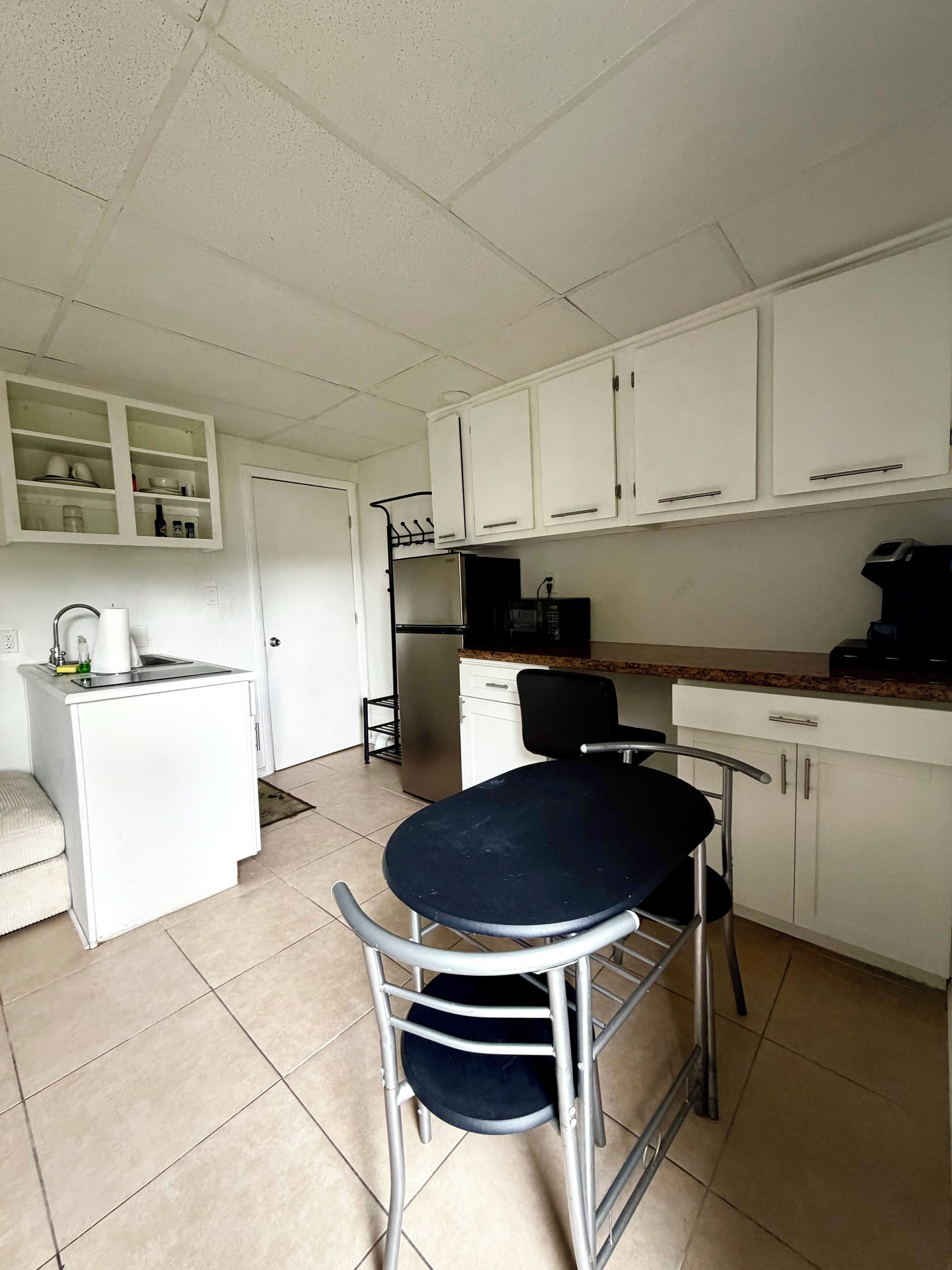 A compact kitchen with white cabinets, a refrigerator, a microwave, and a small dining table with chairs.