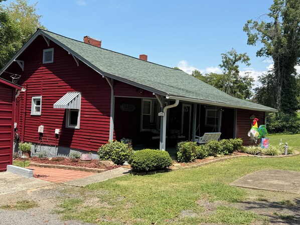 A red wooden house with a porch, number 115, and a rooster decoration.