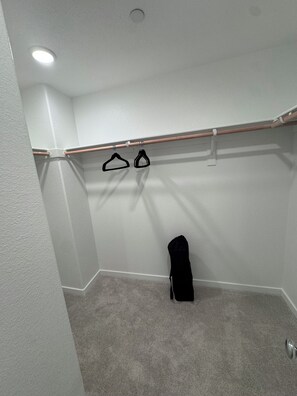 Ein Kleiderschrank mit einer Holzstange und Kleiderbügeln, eine schwarze Tasche am Boden und eine Deckenleuchte.
