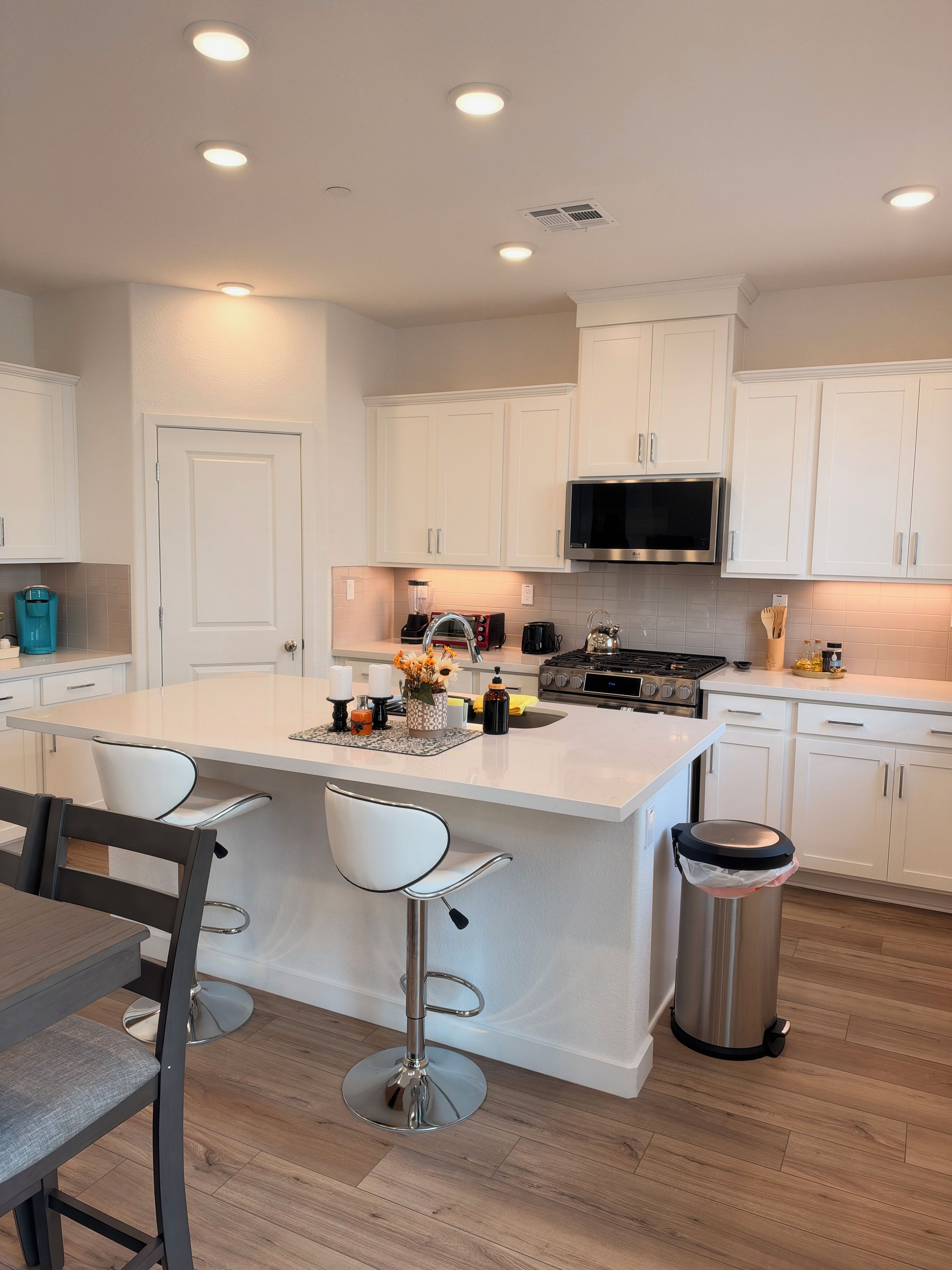 Una cocina moderna con armarios blancos, una isla central con taburetes de bar, un bote de basura de acero inoxidable y un microondas sobre la estufa.