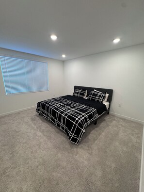 Ein Schlafzimmer mit einem Bett, einem Fenster mit Jalousien und Einbaustrahlern.