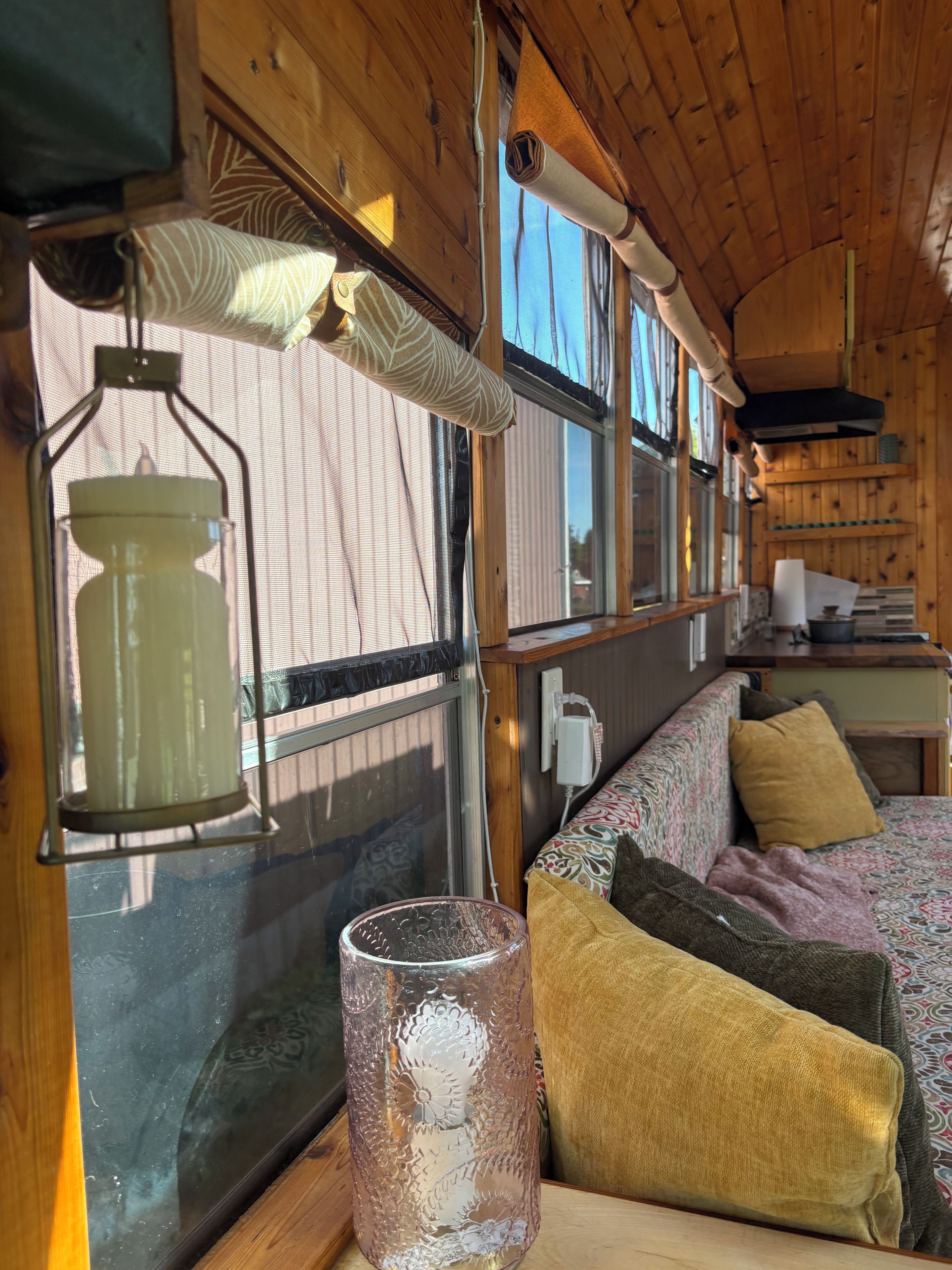 Un intérieur chaleureux avec un plafond en bois, une fenêtre avec des rideaux, un canapé à motifs et un vase en verre.