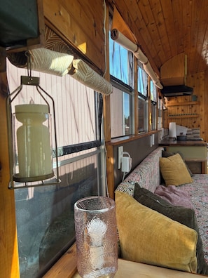 Un intérieur chaleureux avec un plafond en bois, une fenêtre avec des rideaux, un canapé à motifs et un vase en verre.