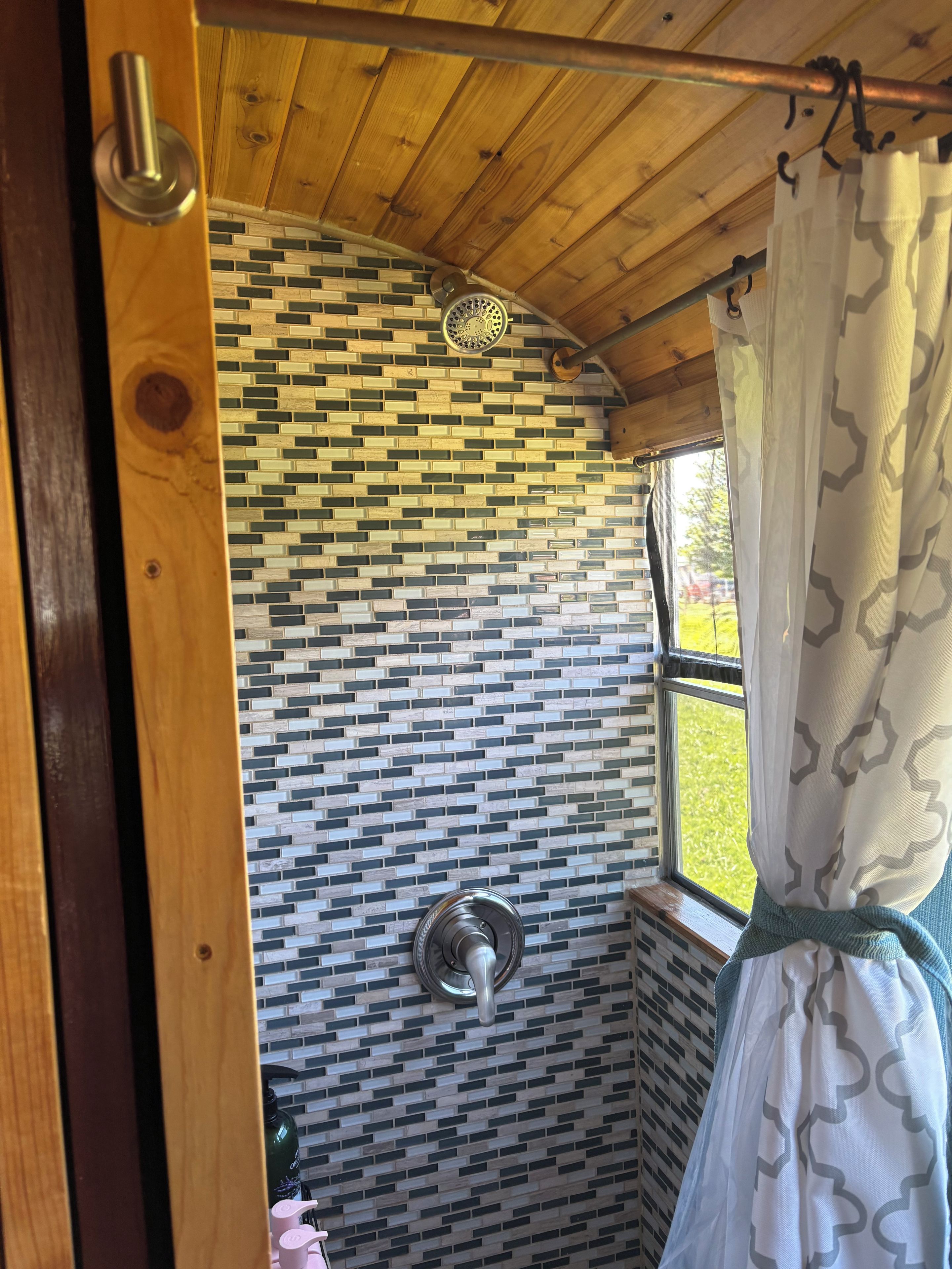 Un baño con pared de azulejos estampados, zona de ducha y ventana con cortina.