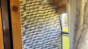 Un baño con pared de azulejos estampados, zona de ducha y ventana con cortina.
