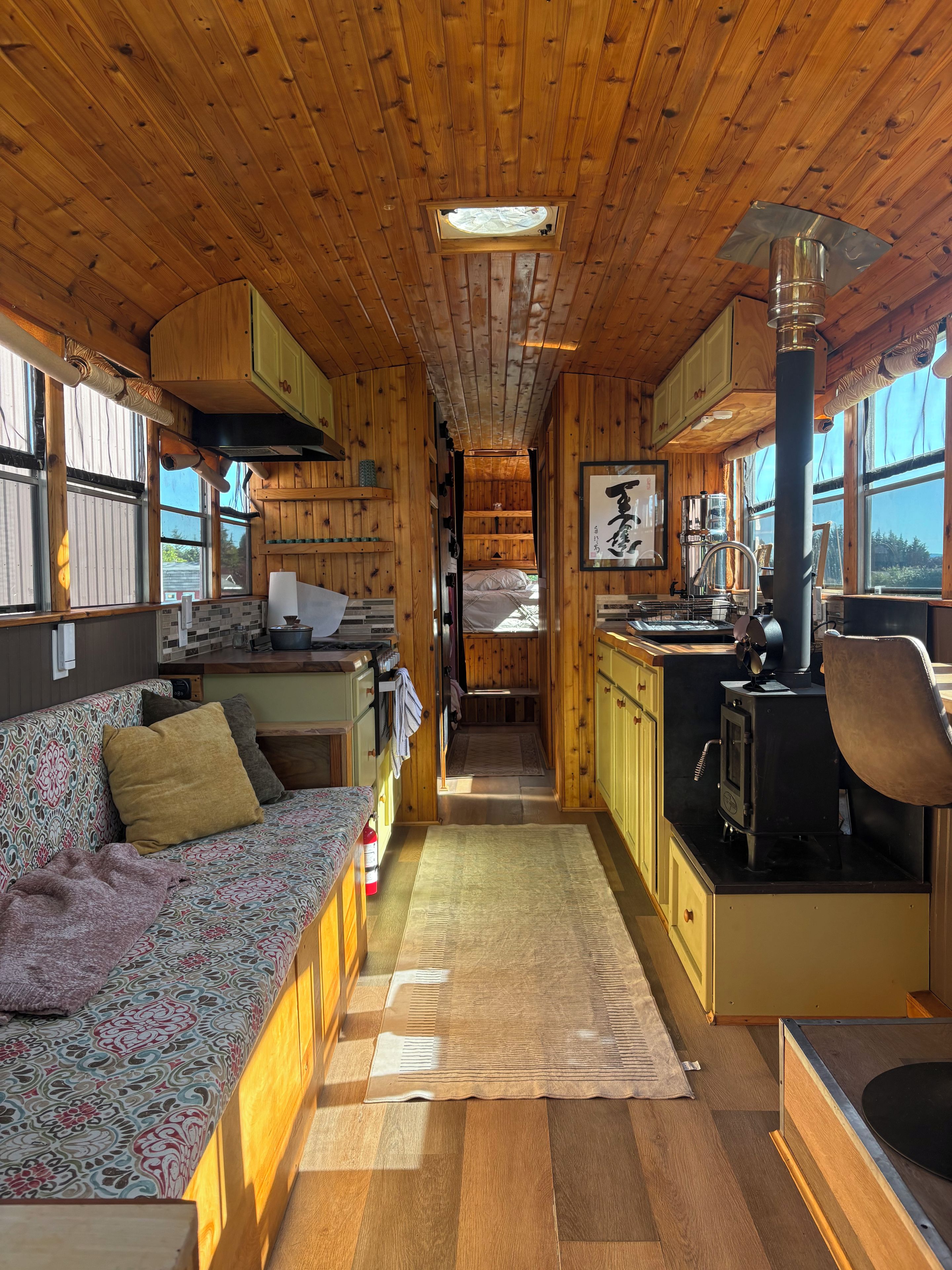Ein gemütliches Blockhauss-Interieur mit Holzbalkendecke, einer Couch, einer Küchenzeile mit Herd und einem Fenster, das für natürliches Licht sorgt.